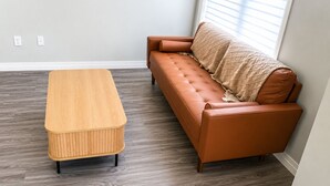 Ein Zimmer mit einer hölzernen Sitzbank und einem braunen Ledersofa vor einer Wand mit einem Fenster.