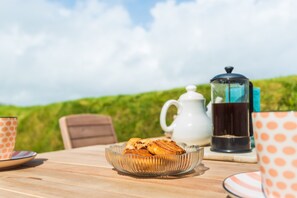 A table with a glass bowl of pastries, a white teapot, a coffee pot, and matching orange and white polka-dotted cups. - Choughs with countryside views and close to Fowey (Bodinnick)