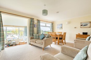 A living room with a sofa, armchairs, a dining table, and chairs. There is a window with curtains, a lamp, and a painting on the wall. - Choughs with countryside views and close to Fowey (Bodinnick)