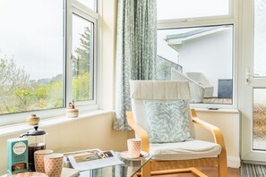 A room with a chair near a window, a small table with a book and a cup, and a view of a staircase outside. - Choughs with countryside views and close to Fowey (Bodinnick)