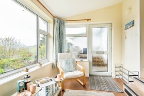 A cozy room with a large window, a chair, a small table, and a door leading outside. - Choughs with countryside views and close to Fowey (Bodinnick)
