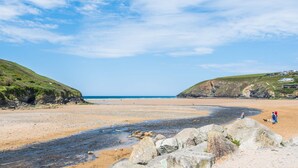 A beach with rocky outcrops, a clear sky, and distant hills. - Well Cottage - Three Bedroom Cottage, Sleeps 6 (Trevarrian)