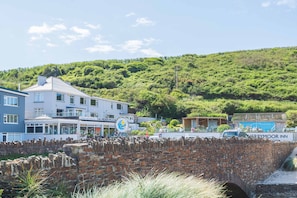 A coastal town with a prominent brick bridge, a hotel named 'Ferrymoor Inn,' and lush green hills in the background. - Well Cottage, near dog friendly beach Mawgan Porth (Trevarrian)
