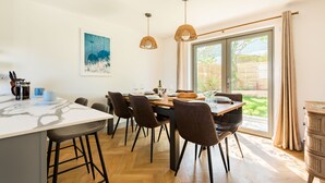 A modern kitchen with a marble countertop, wooden flooring, and a dining area with chairs and a table. - Well Cottage - Three Bedroom Cottage, Sleeps 6 (Trevarrian)