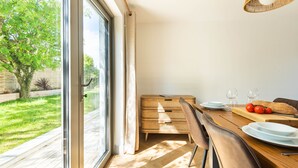 A dining area with a table set for two, a wicker lamp, and a view of a garden through a glass door. - Well Cottage - Three Bedroom Cottage, Sleeps 6 (Trevarrian)
