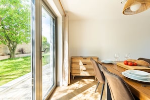 A dining area with a table set for two, a wicker lamp, and a view of a garden through a glass door. - Well Cottage, near dog friendly beach Mawgan Porth (Trevarrian)