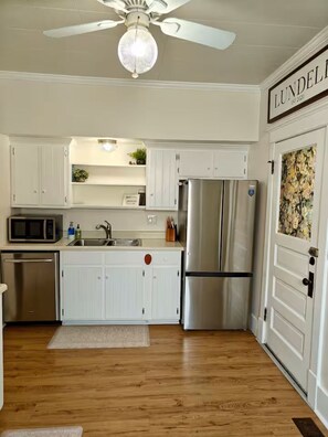 A kitchen with white cabinets, stainless steel appliances, a ceiling fan, and a door with a floral pattern. - Cozy 3 Bedroom Home in Omaha (Omaha)
