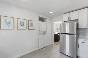 A modern kitchen with white cabinets, a stainless steel refrigerator, and a washing machine.