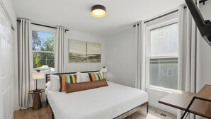 A bedroom with a bed, bedside table, lamp, and a view of the outdoors. - Near EMU & Ann Arbor | King Bed, AC & WiFi (Ypsilanti)