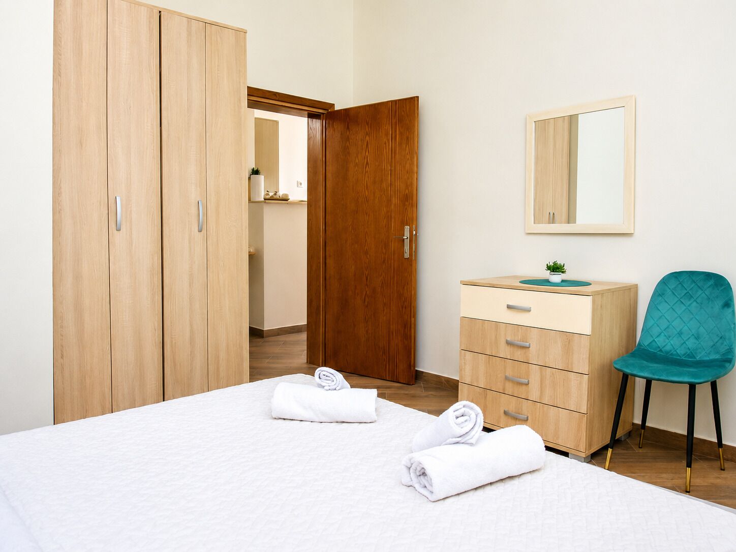 Una camera da letto con un letto, un armadio in legno, una cassettiera, una sedia e uno specchio.