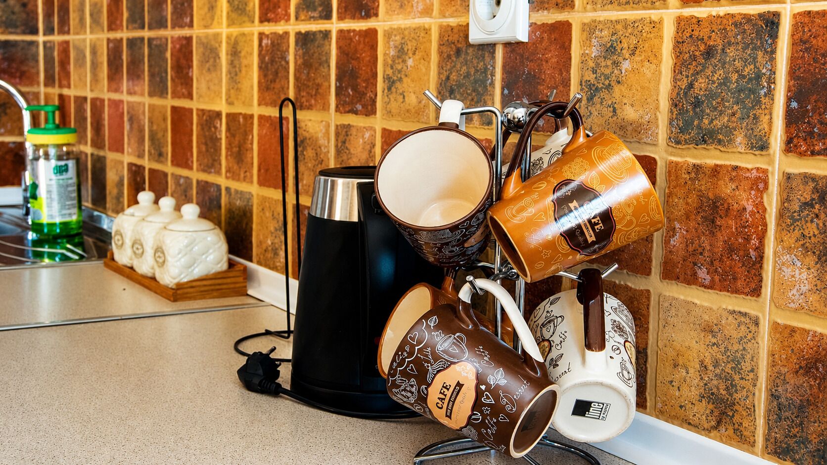 Una cucina con una macchina da caffè, tazze e una bottiglia di detersivo per piatti sul piano di lavoro.