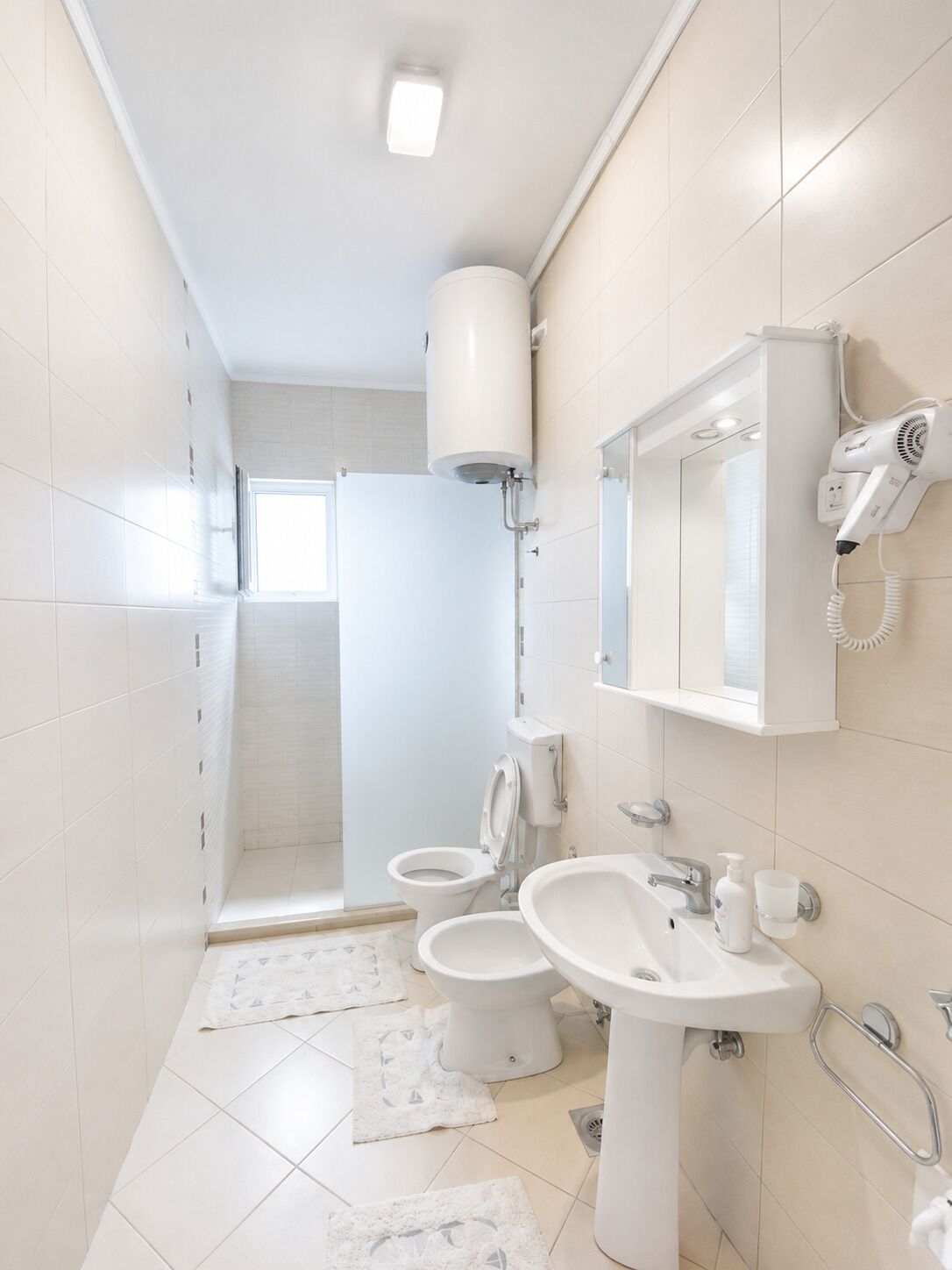Une salle de bain moderne équipée de toilettes, d’un bidet, d’un lavabo et d’un sèche-cheveux fixé au mur.