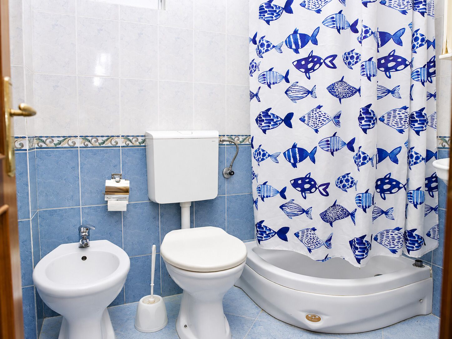 Un baño con inodoro, bidé y cortina de ducha con estampado de peces.