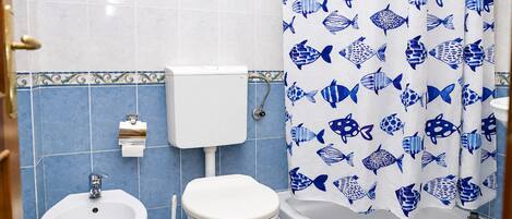 Un baño con inodoro, bidé y cortina de ducha con estampado de peces.