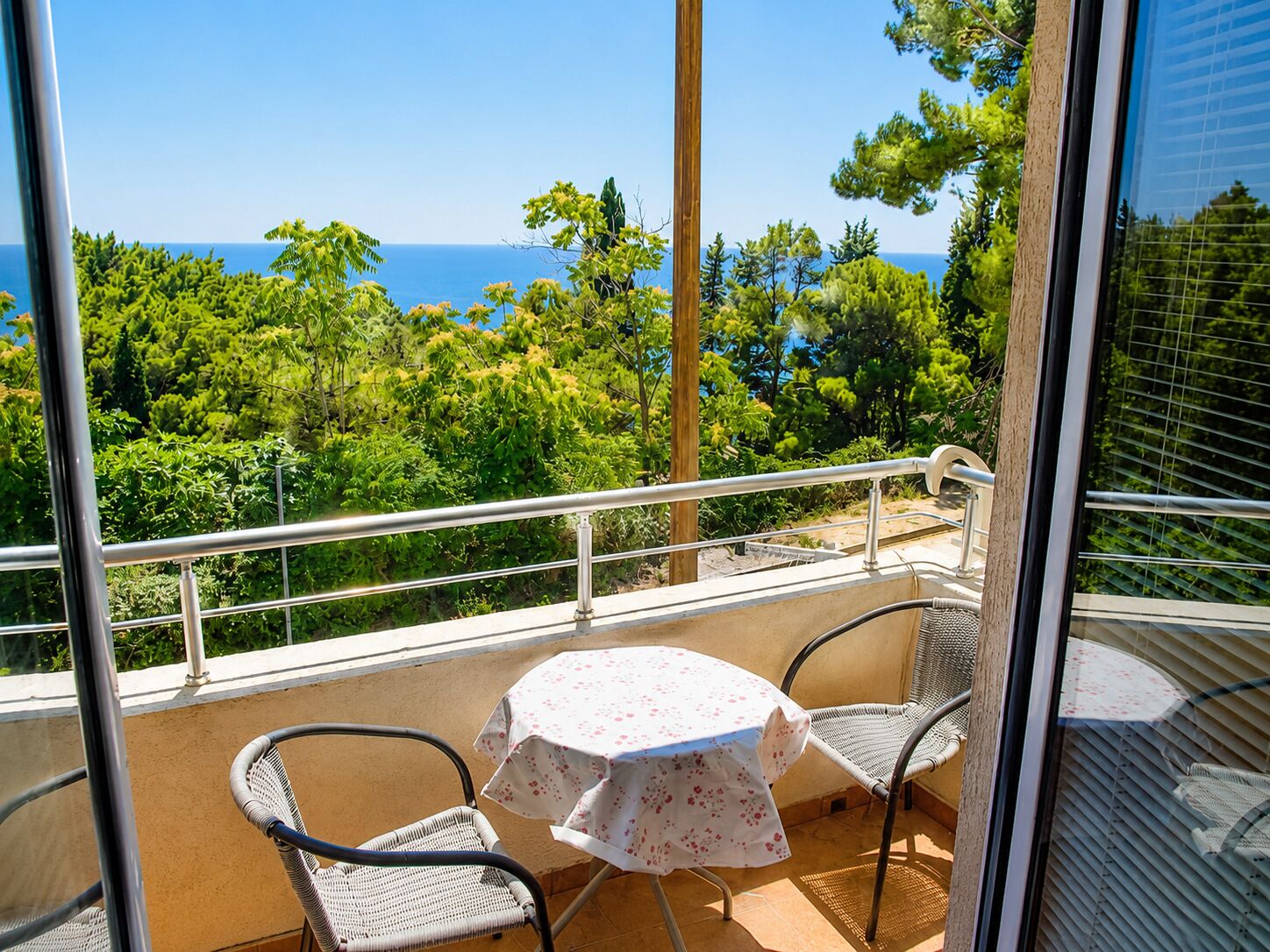 Un balcón con mesa y sillas, con vista a un paisaje de árboles y el mar.