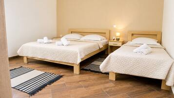 A hotel room with two beds, a wooden floor, a striped rug, and a nightstand with a lamp.