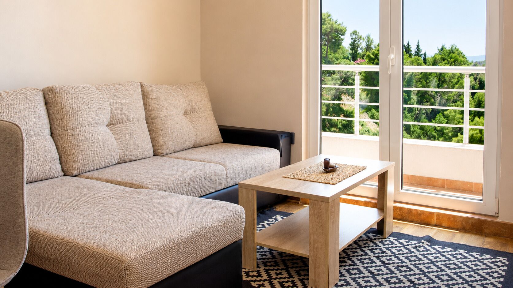 Een moderne woonkamer met een beige bank, een houten salontafel en een kamerkleed met dessin.