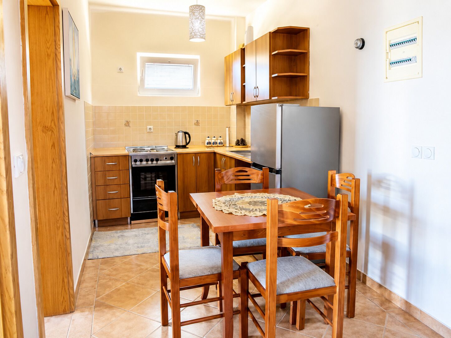 A compact kitchen with a stove, oven, refrigerator, wooden cabinets, and a dining table with chairs.