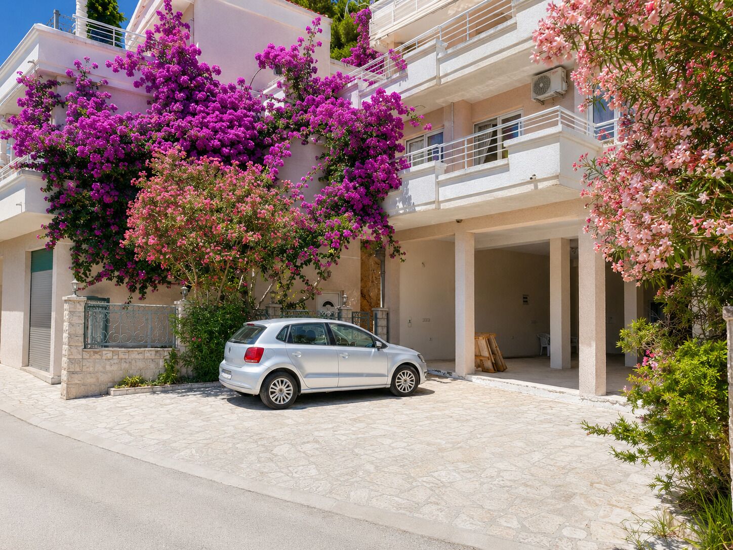 A modern building with a white facade, a parked car, and vibrant purple bougainvillea flowers.