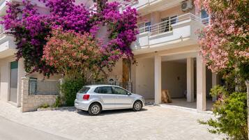 Ein modernes Gebäude mit weißer Fassade, einem geparkten Auto und üppigen, violetten Bougainvillea-Blüten.