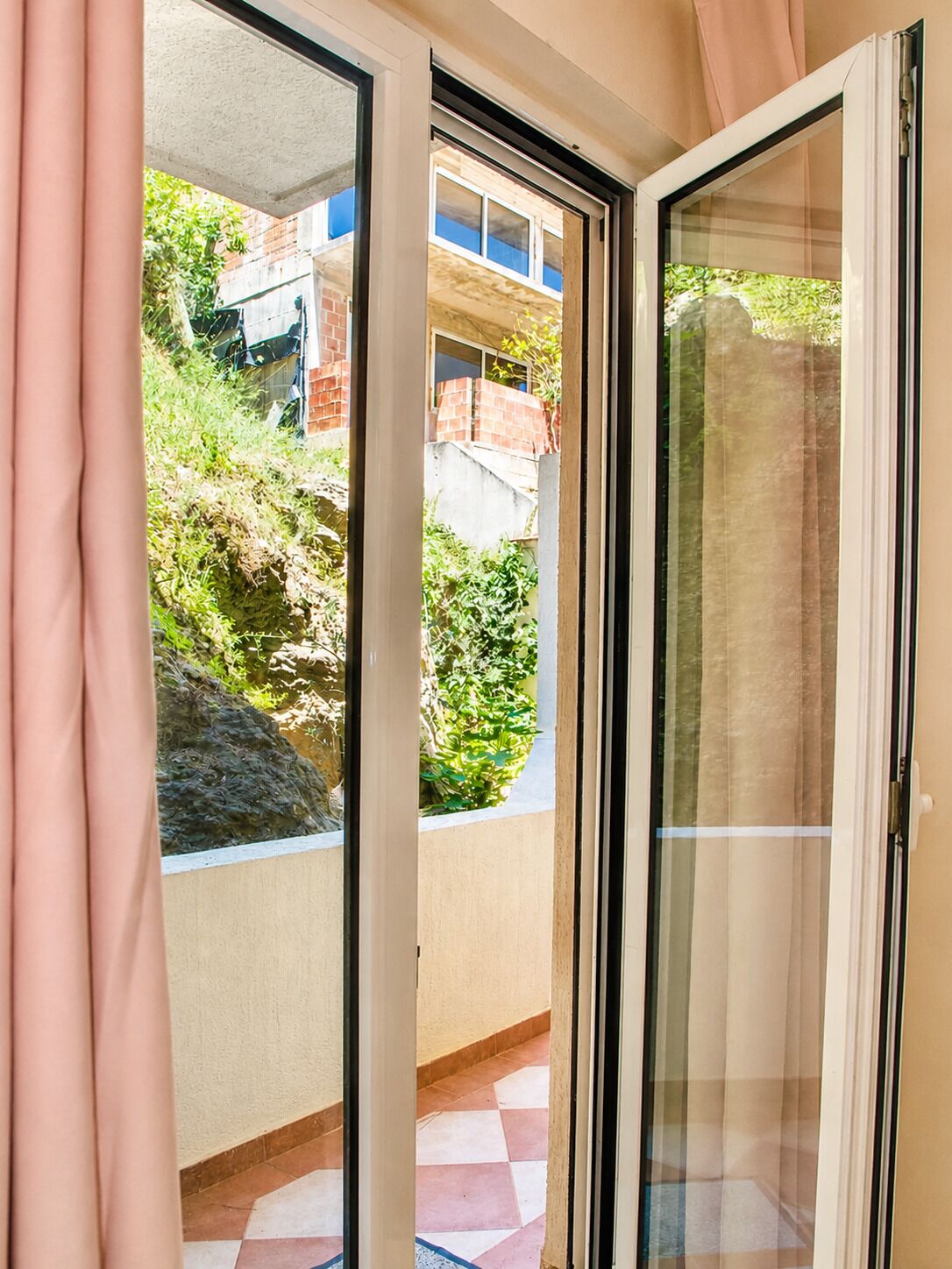 A sliding glass door leading to a balcony with a view of a hillside and a building in the background.