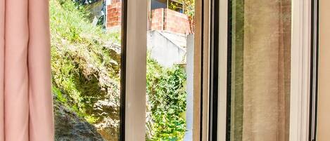 A sliding glass door leading to a balcony with a view of a hillside and a building in the background.