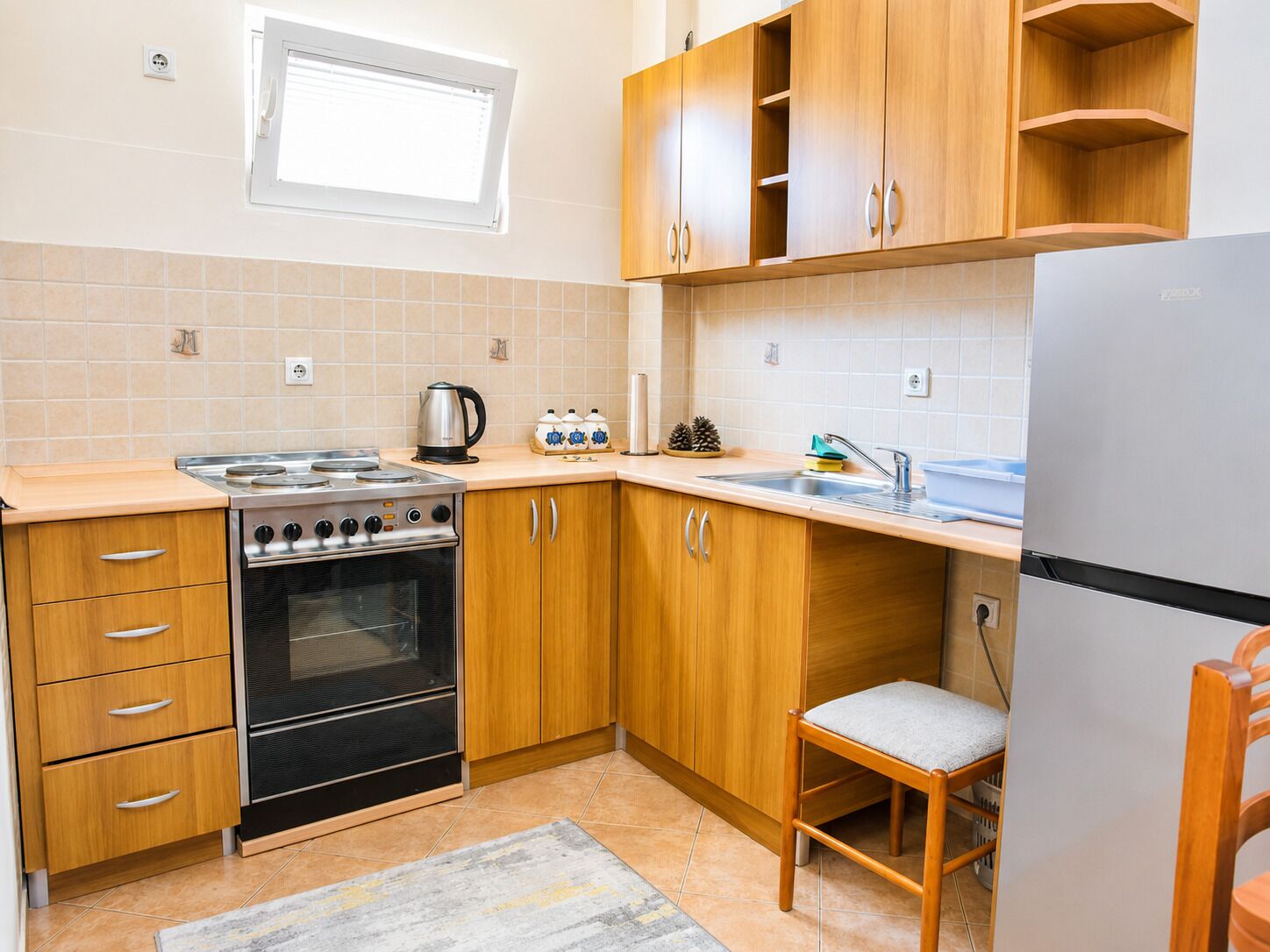A kitchen with wooden cabinets, a stove, a sink, and a chair.