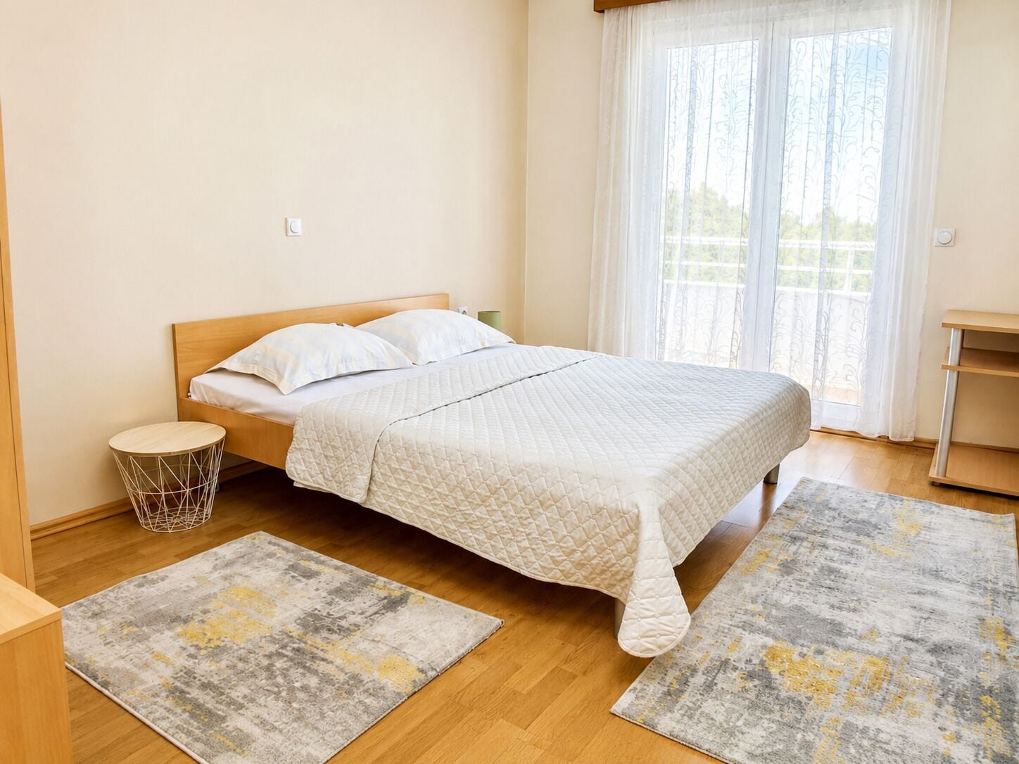A bedroom with a bed, two rugs, a bedside table, and a window with curtains.