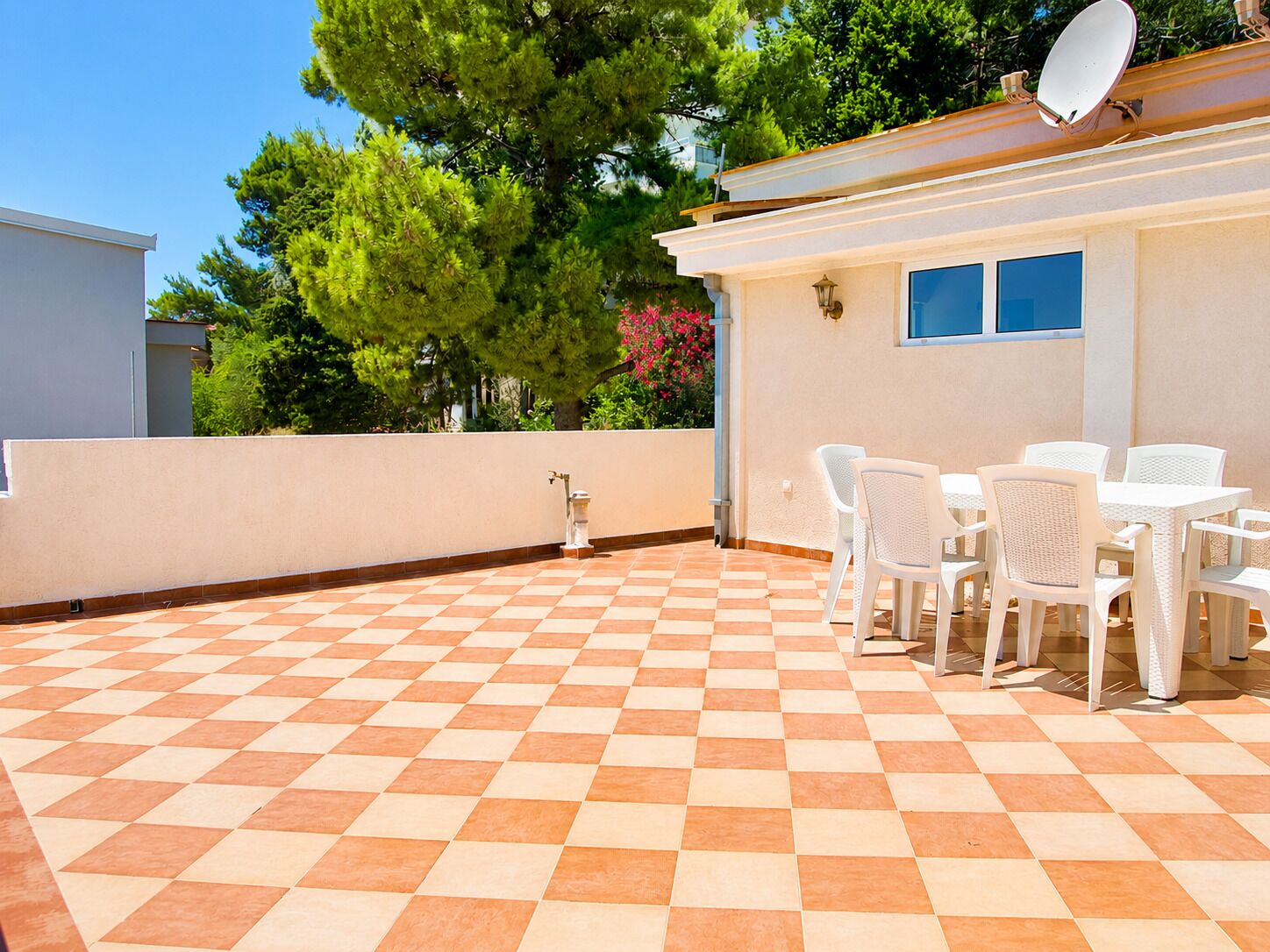 Un patio con piso a cuadros, sillas blancas y una mesa.