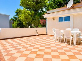 Un patio con piso a cuadros, sillas blancas y una mesa.