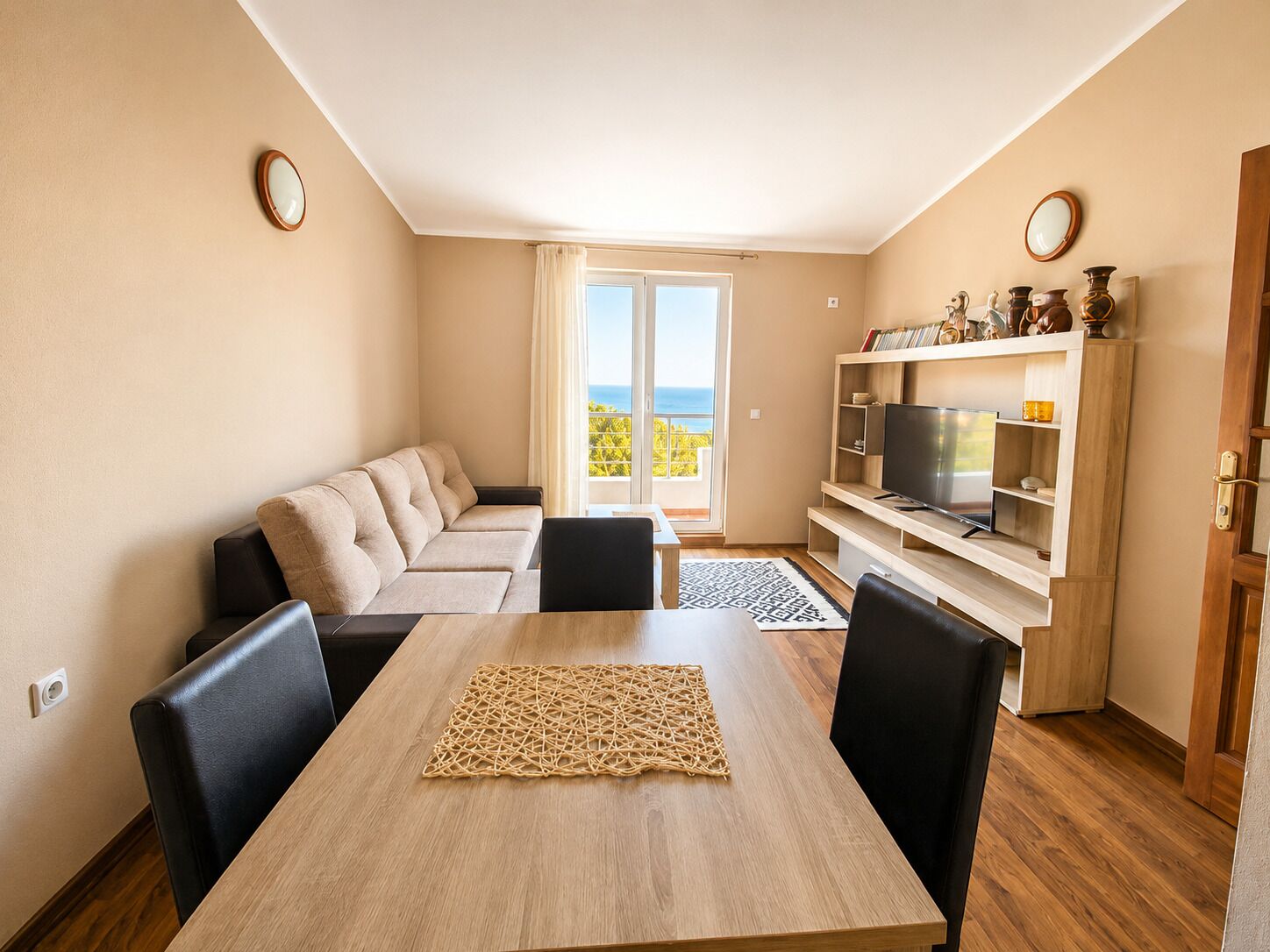 A modern living room with a sofa, dining table, chairs, a TV, and a balcony with a view.