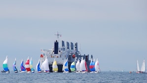 Un barco grande con varios veleros de colores en primer plano.