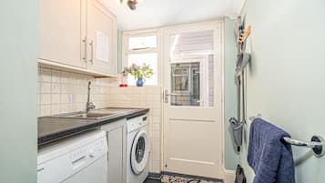 Cocina compacta con lavadora, un lavamanos y una ventana con planta.