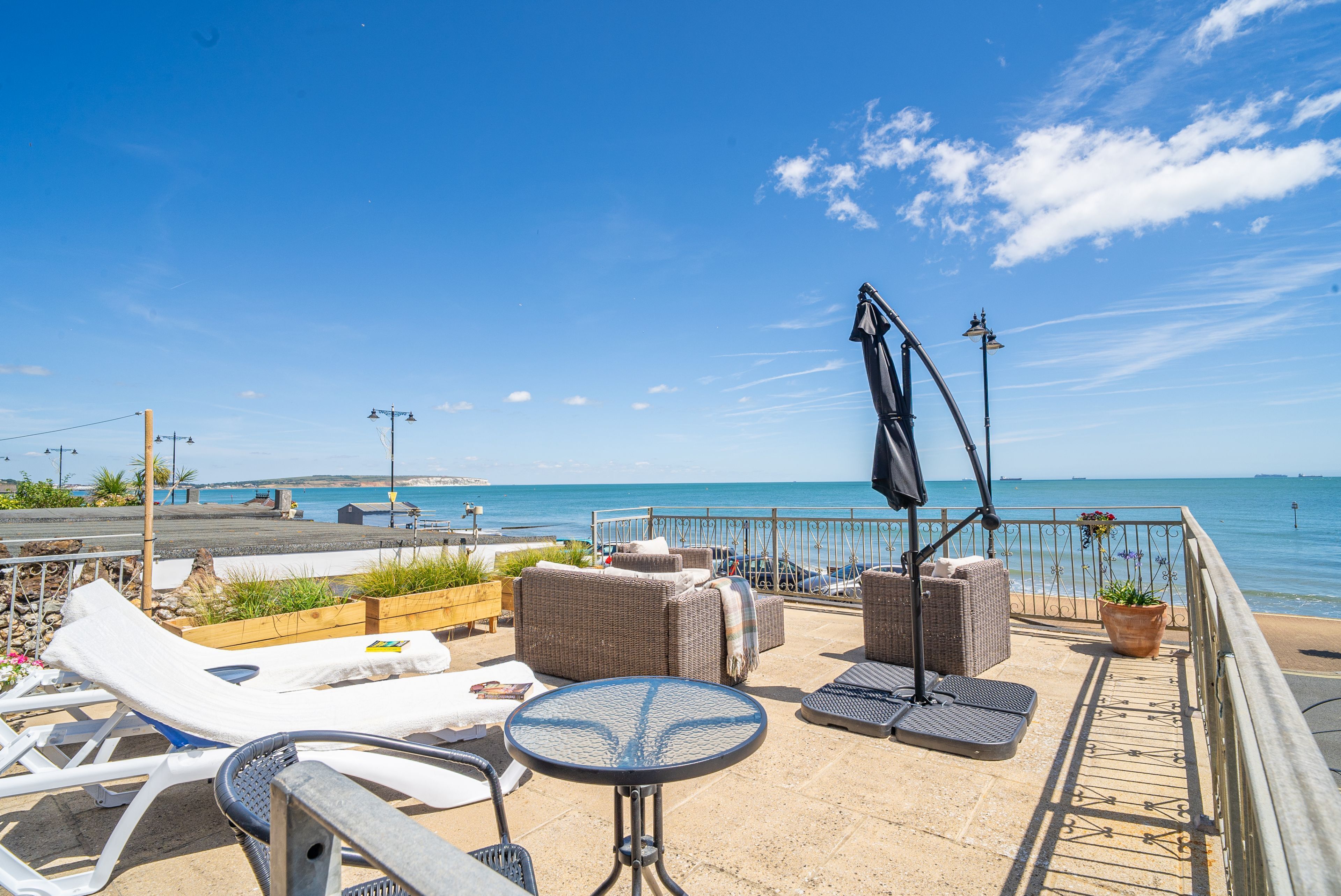 Eine Terrasse mit Lounge-Möbeln, einem Tisch und einem Topfpflanzen, die auf das Meer blickt.