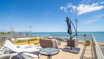 Eine Terrasse mit Lounge-Möbeln, einem Tisch und einem Topfpflanzen, die auf das Meer blickt.