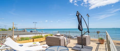 A terrace with lounge chairs, a table, and a potted plant overlooking the sea.