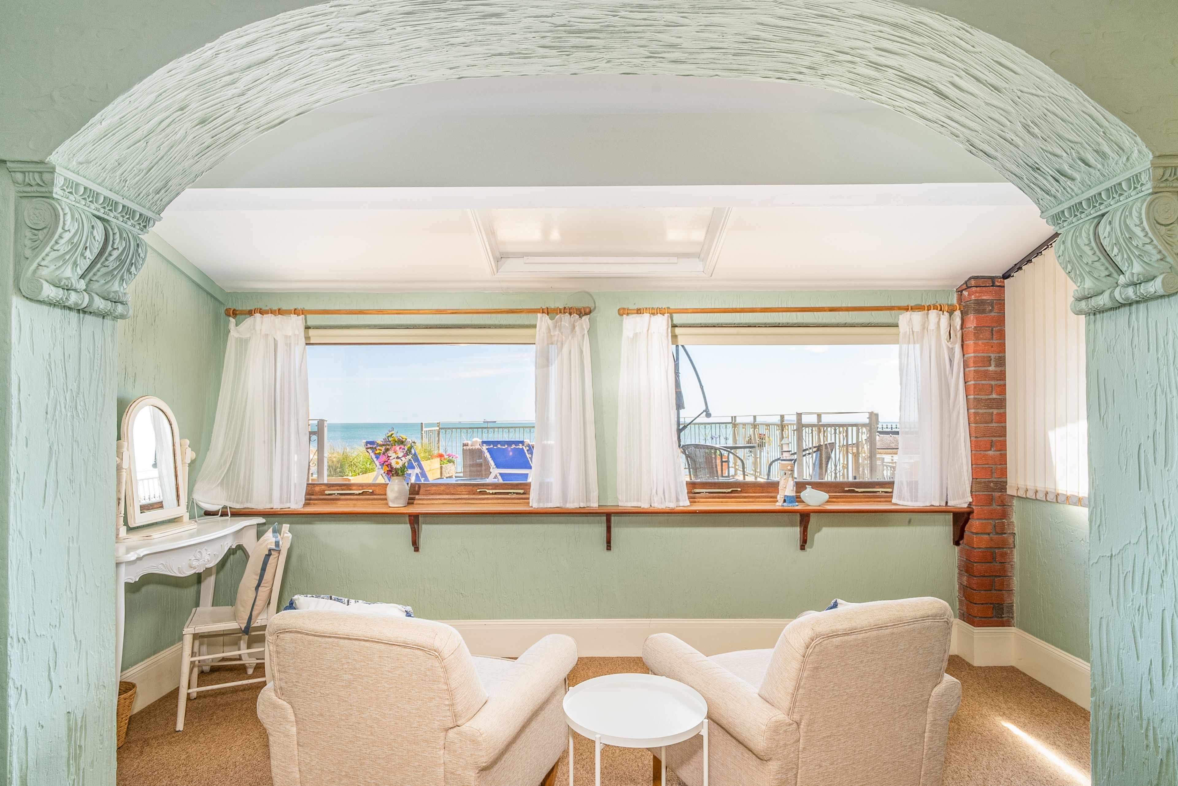 A room with a view of the sea, featuring two chairs, a small table, and a window with curtains.