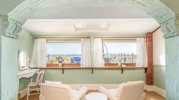 A room with a view of the sea, featuring two chairs, a small table, and a window with curtains.