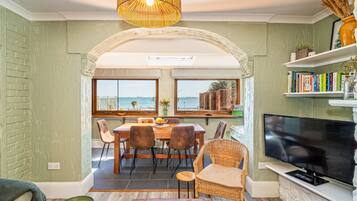A dining area with a view of the sea, a television, and a bookshelf.