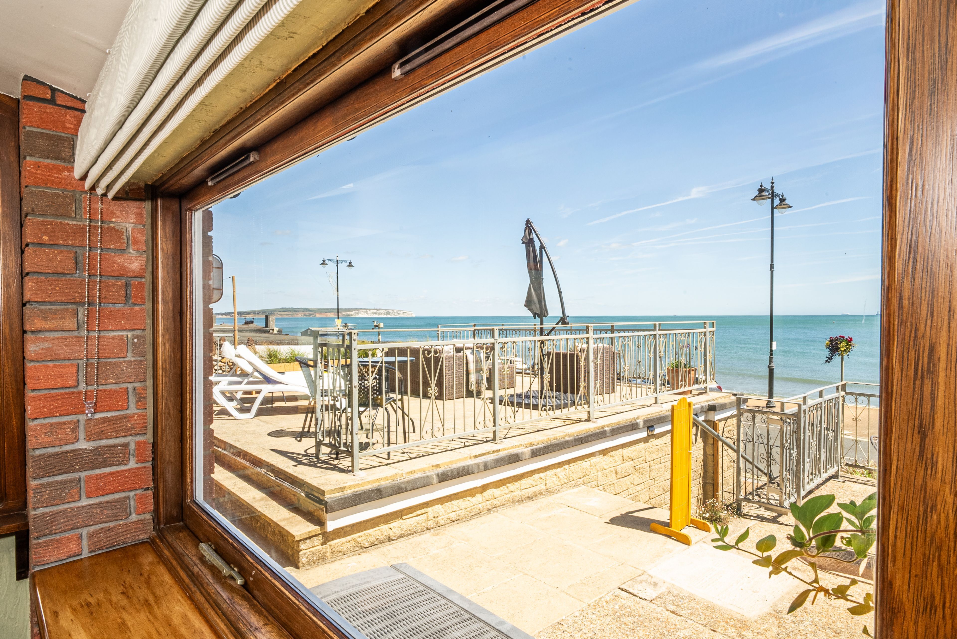 A balcony with a view of the sea, a brick wall, and outdoor furniture.