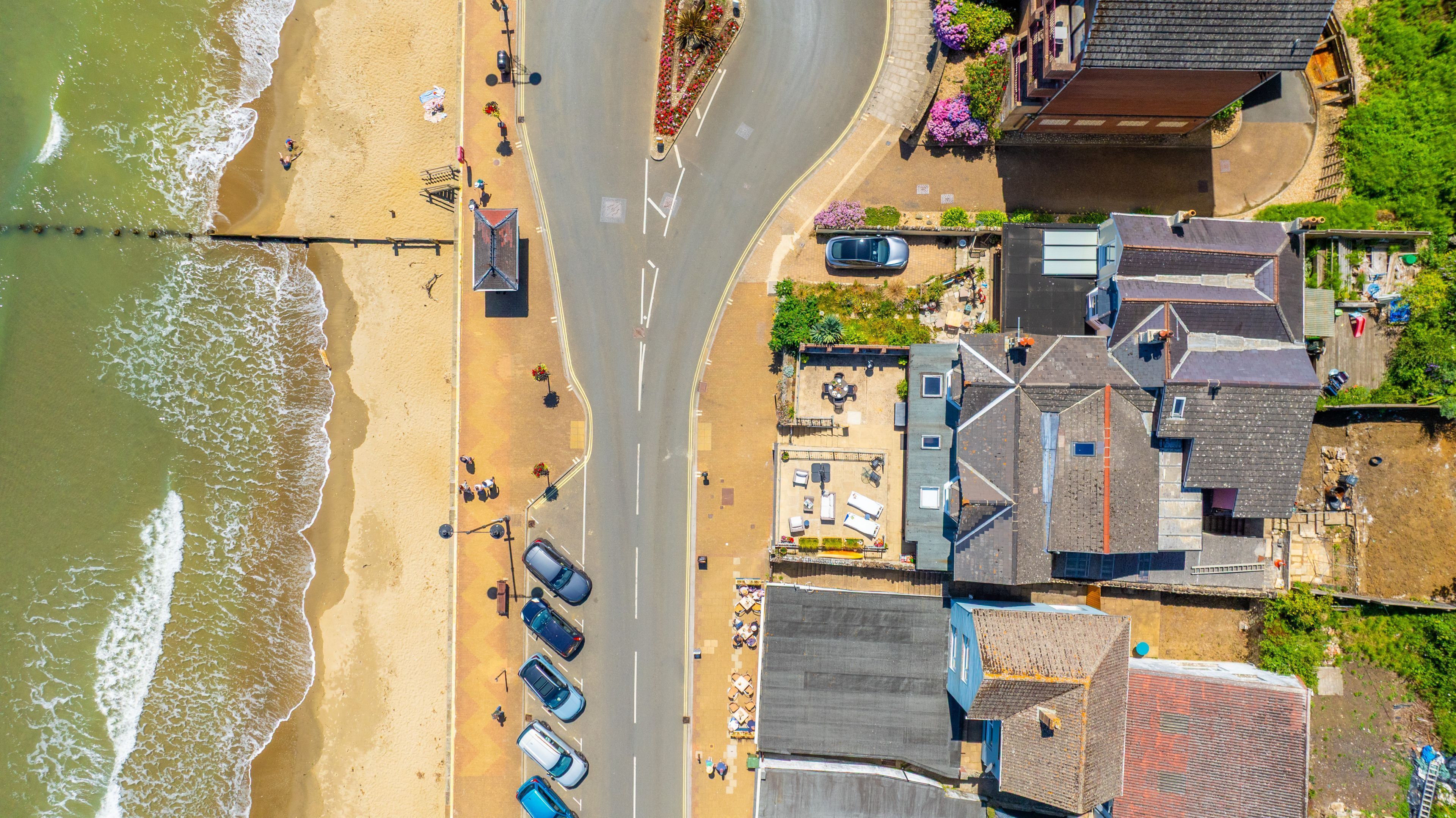 Vista aérea de una zona costera con playa, coches aparcados y edificios con tejados inclinados.