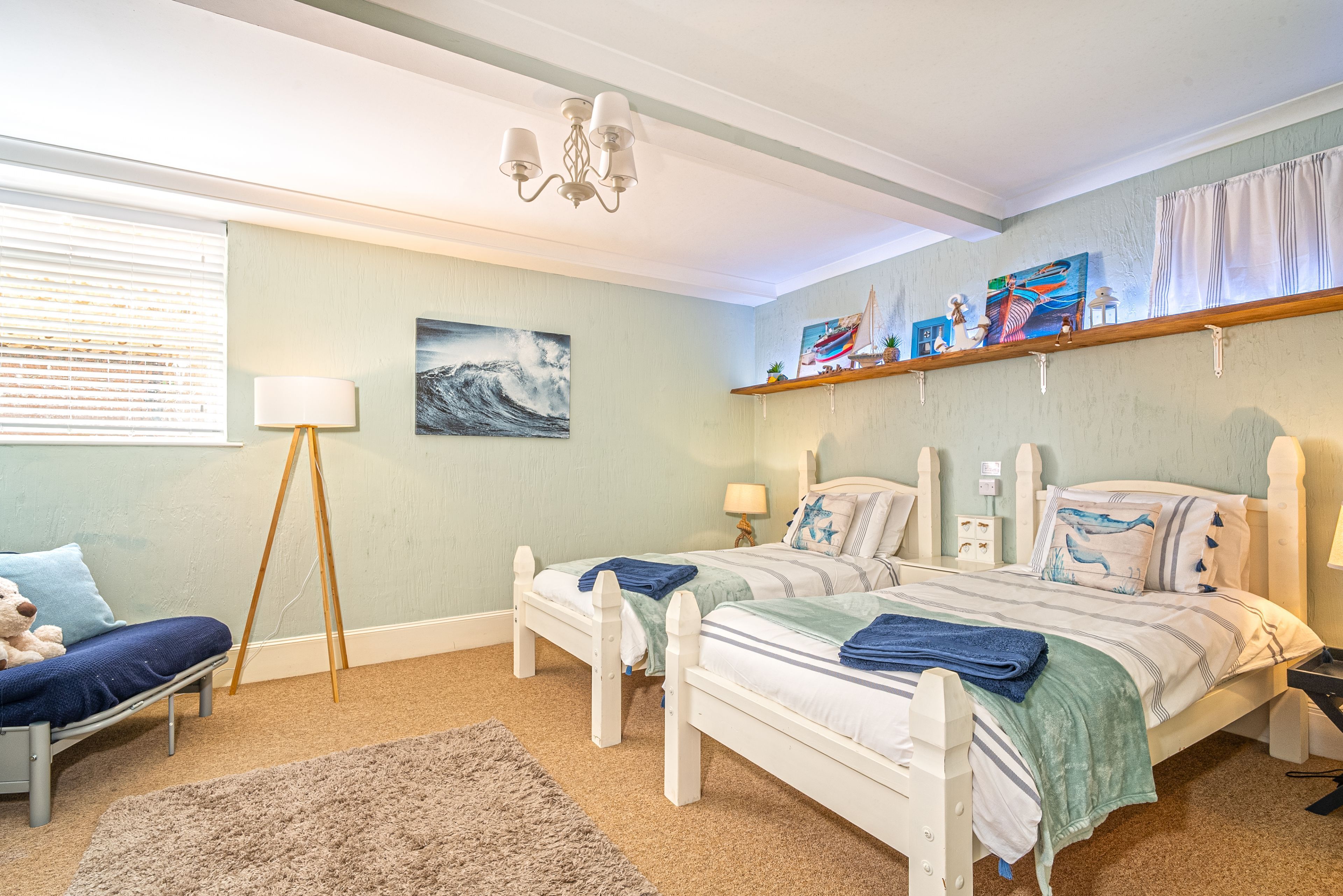 Une chambre avec deux lits, une table de chevet, une lampe, une chaise, un tapis et des œuvres d’art accrochées aux murs.