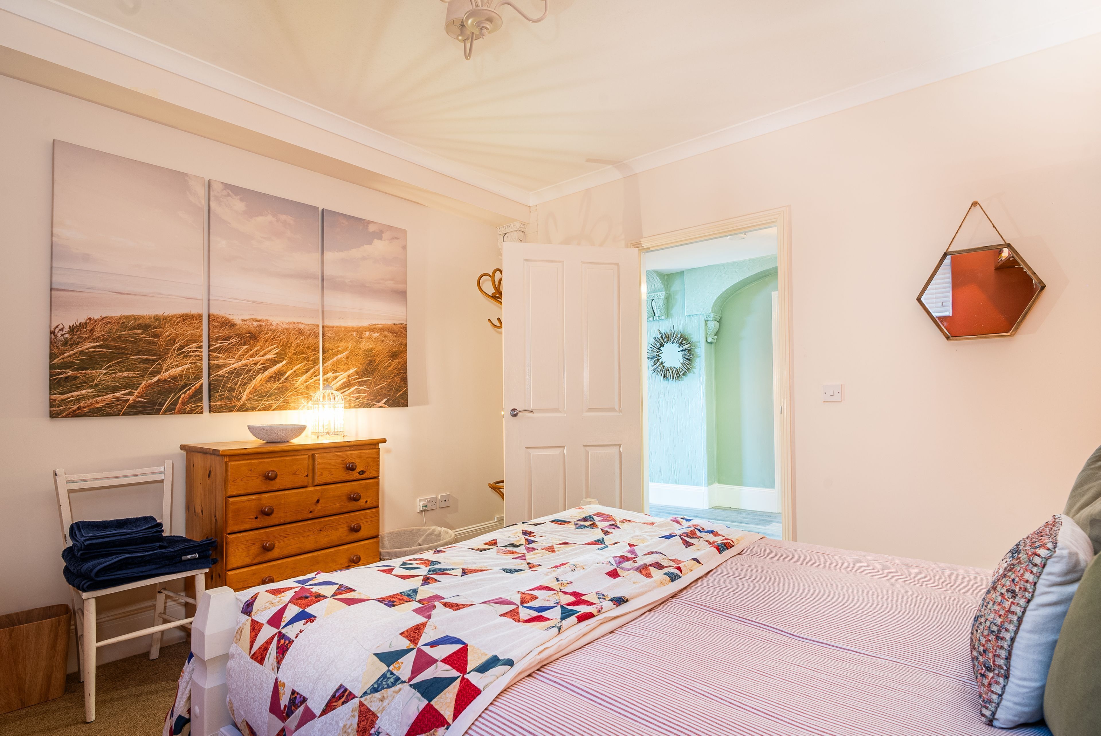 Un dormitorio con cama, cómoda, mesita de noche, lámpara y espejo en la pared.