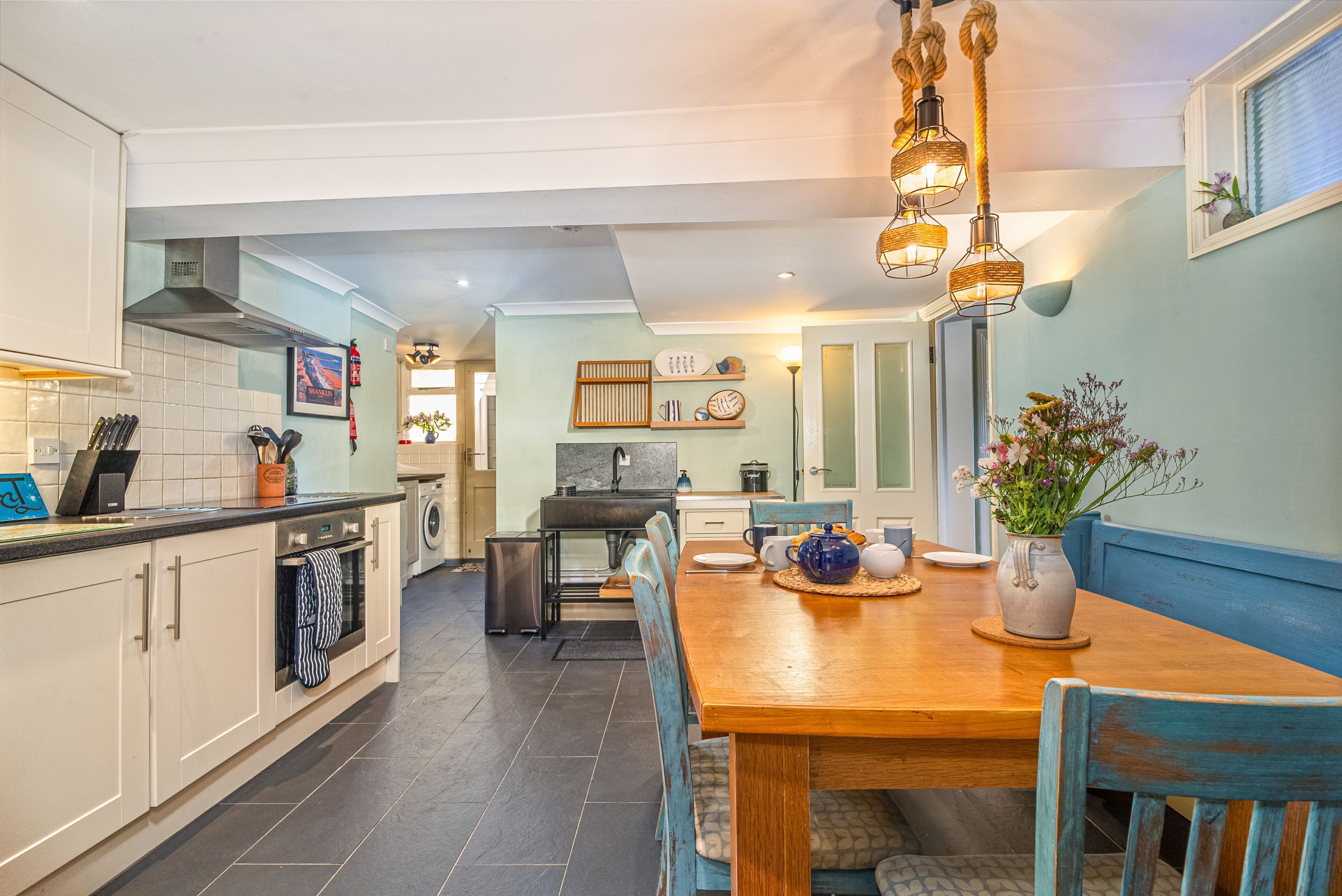 A modern kitchen with a dining area, featuring a wooden table and chairs, a built-in oven, and a large window.