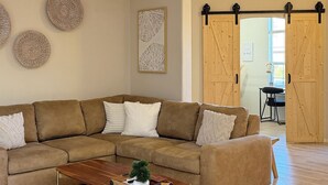 A living room with a sectional sofa, a wooden coffee table, a ceiling fan, and a sliding barn door. - 4-bedroom house in Sedona with hot tub, firepit & grill - walk to hiking trails (Sedona)