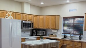 A modern kitchen with wooden cabinets, a white refrigerator, a built-in oven, a microwave, and a large island with two bar stools. - 4-bedroom house in Sedona with hot tub, firepit & grill - walk to hiking trails (Sedona)