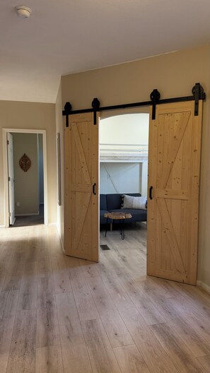 Ein geräumiges Zimmer mit Holzboden, einer Schiebetür im Bauernhausstil, einer Couch und einem kleinen Tisch.