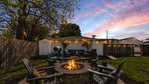 Ein Garten mit Feuerstelle aus Stein, Gartenmöbeln und Lichterketten.