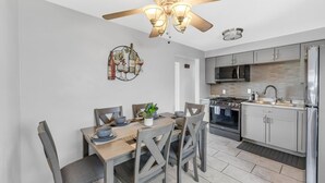 Eine moderne Küche mit Edelstahlgeräten, einem Essbereich mit Holztisch und -stühlen sowie einem Deckenventilator.