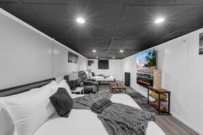 Una habitación de hotel moderna con una cama, dos zonas de estar, un televisor y una chimenea.